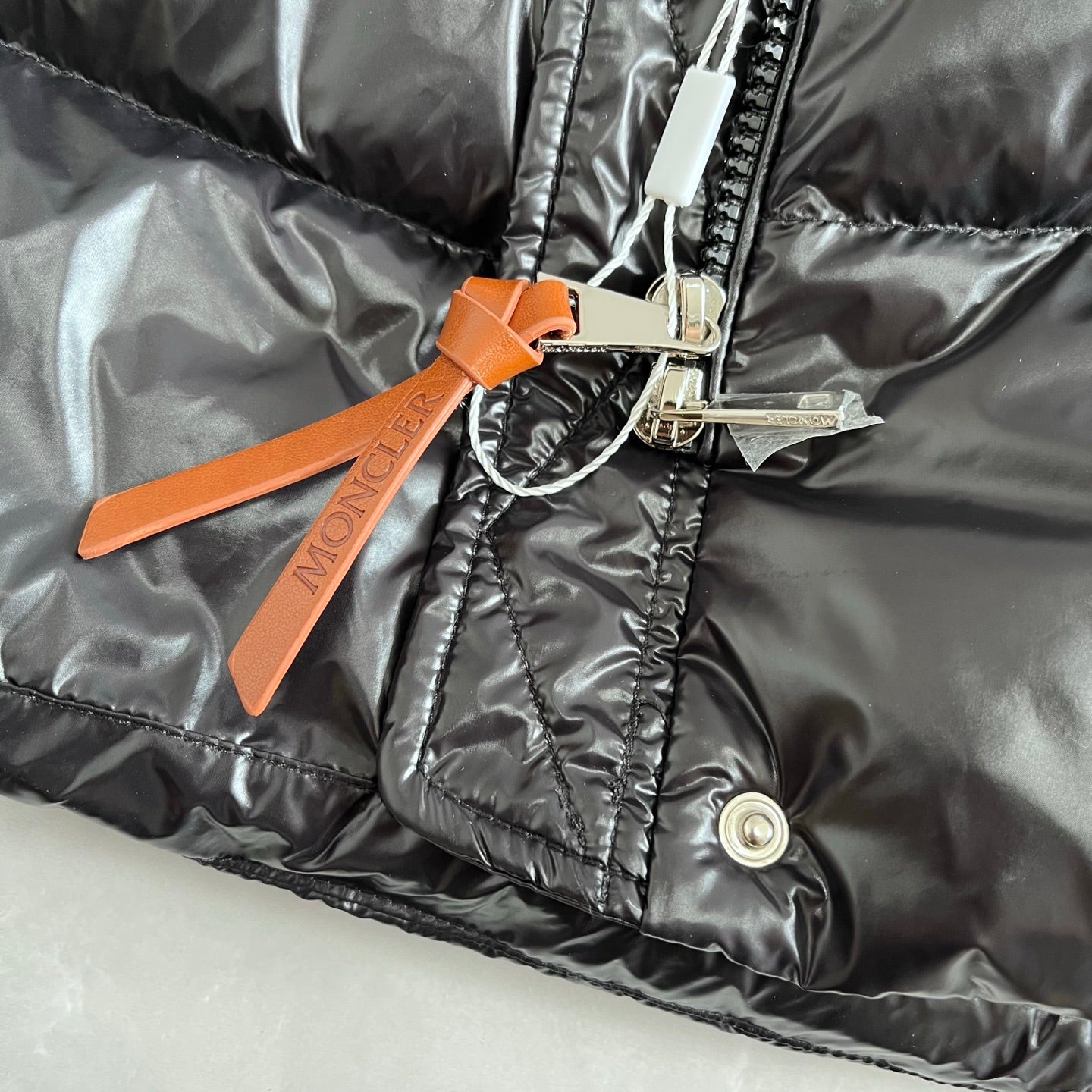 Orange Moncler logo tag on dark gray puffer jacket cuff with snap button