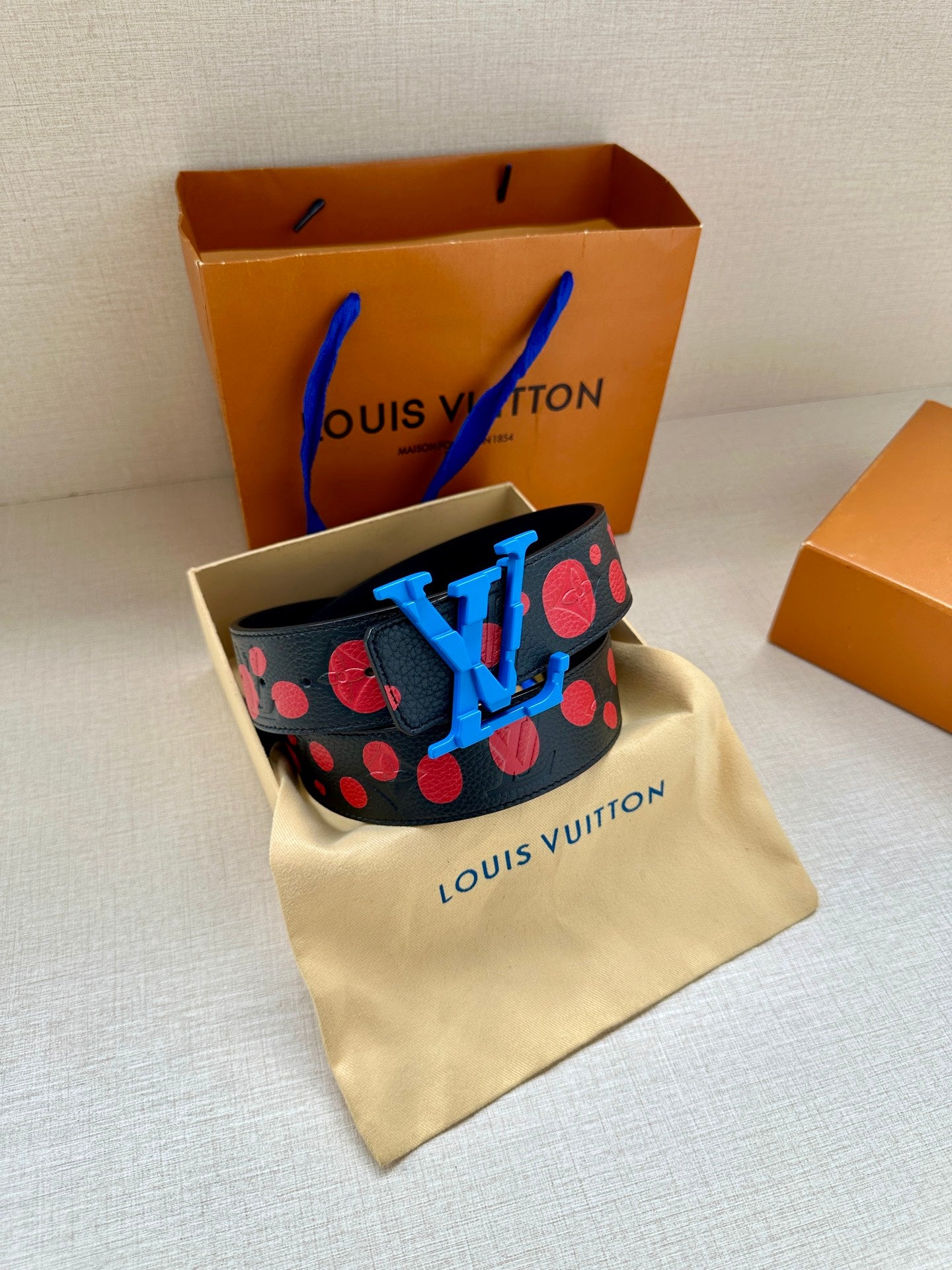 Dark navy leather belt with red dot pattern and blue LV buckle on fabric pouch