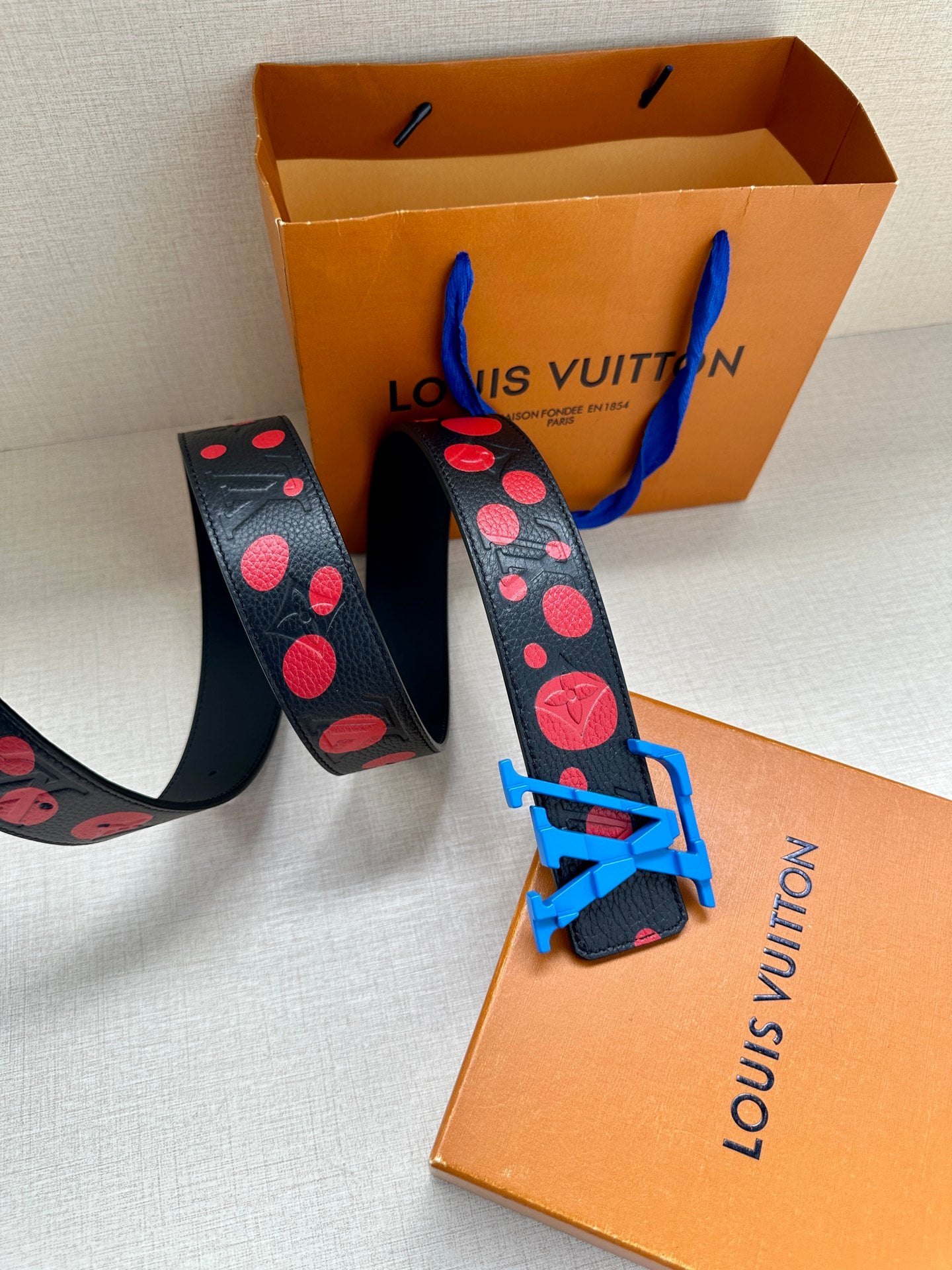 Dark navy leather belt with red dot print and blue LV buckle close-up