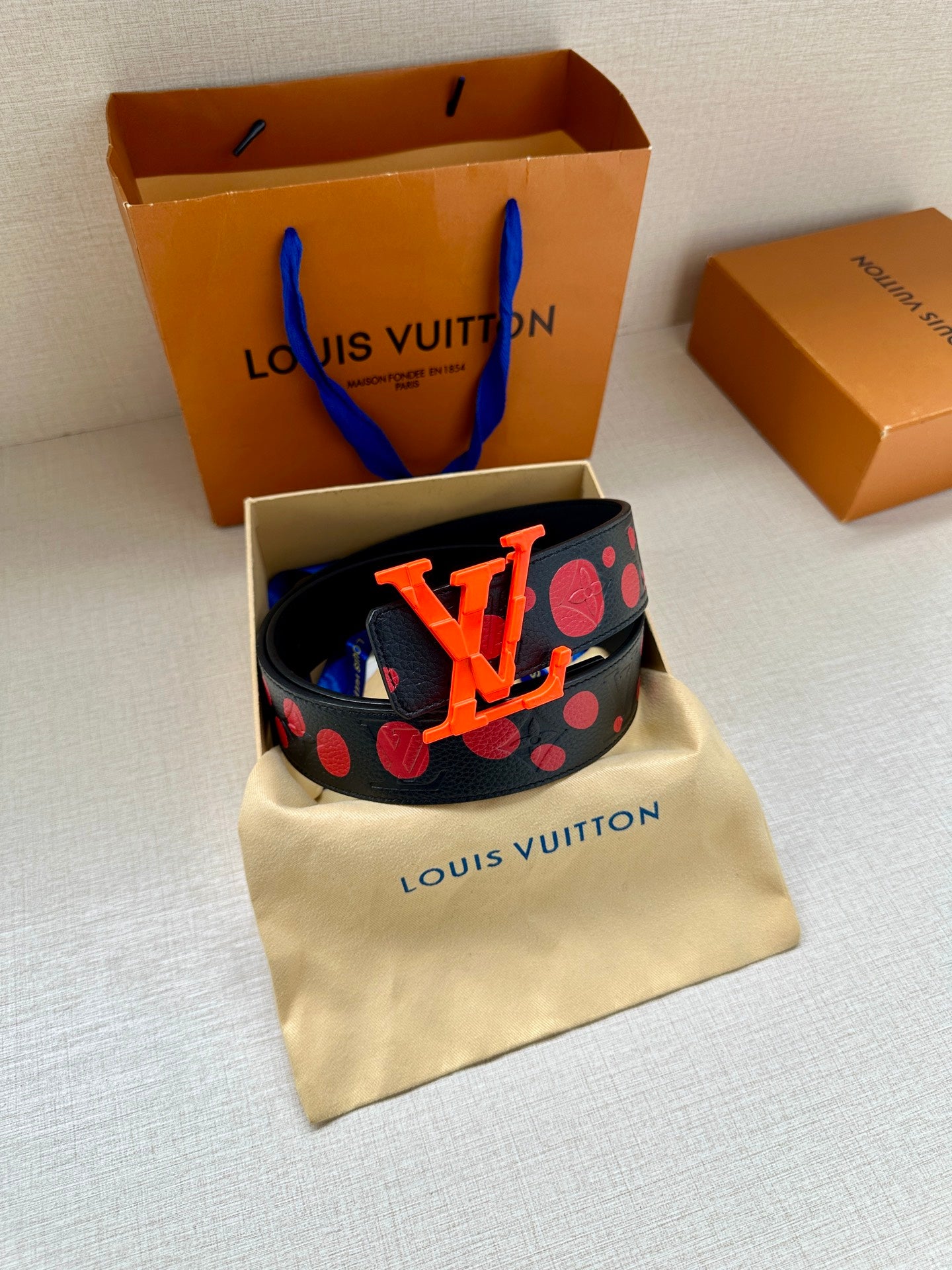 Designer belt on pouch: navy strap with red circles and orange LV logo buckle