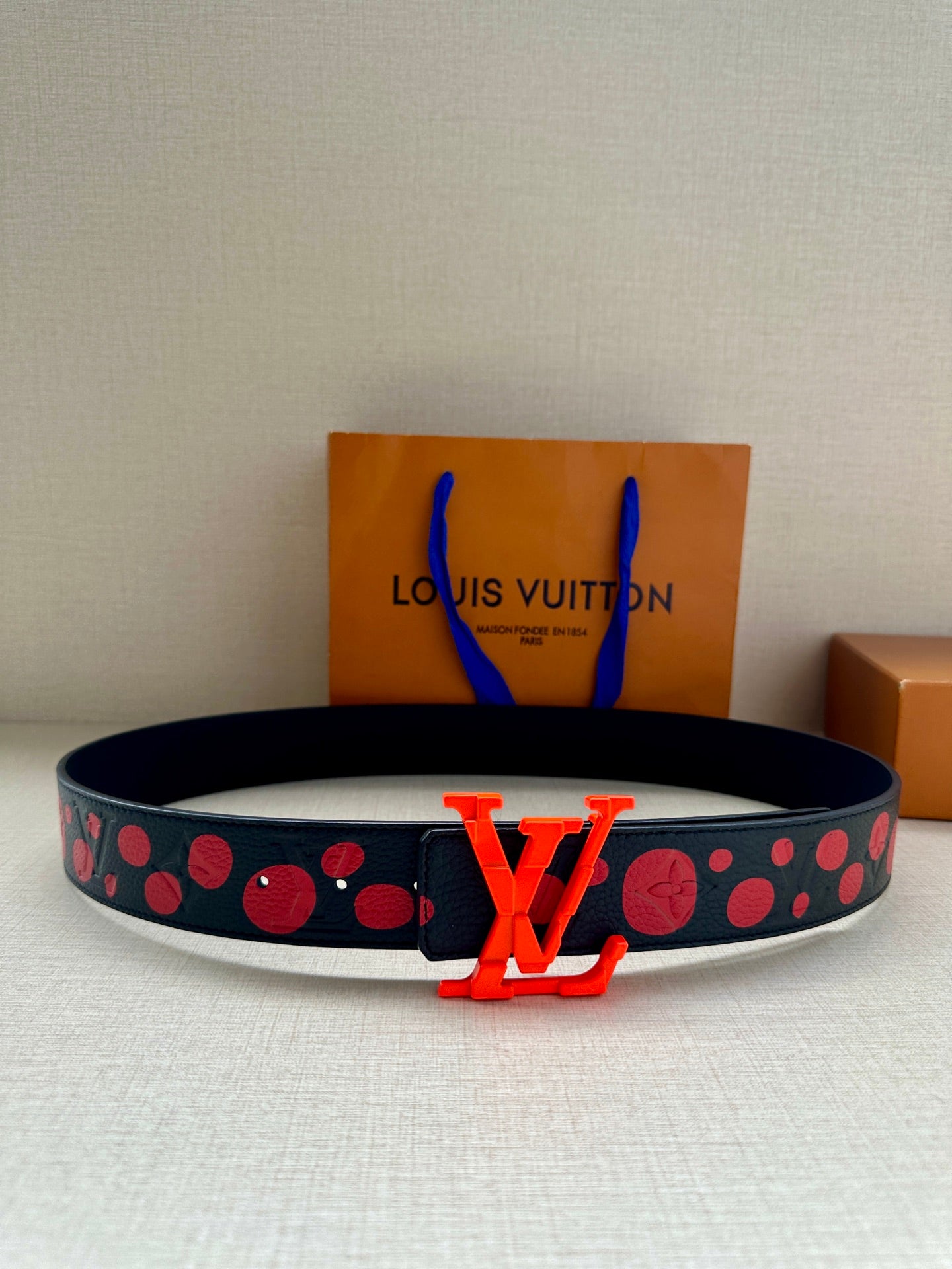 Louis Vuitton belt with dark strap and red studded dot pattern, orange LV buckle