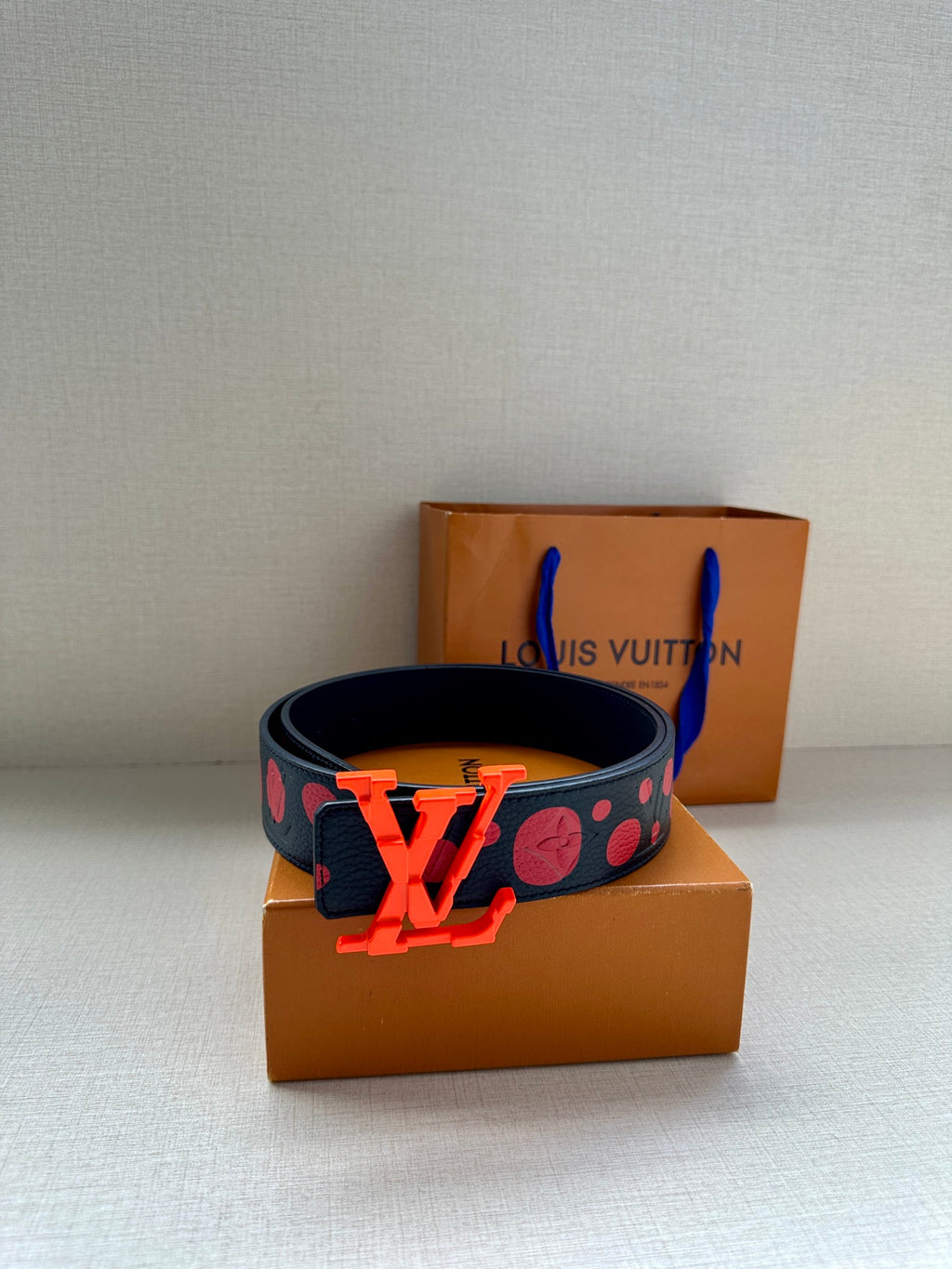 Designer belt with navy patterned strap and oversized orange LV buckle, boxed