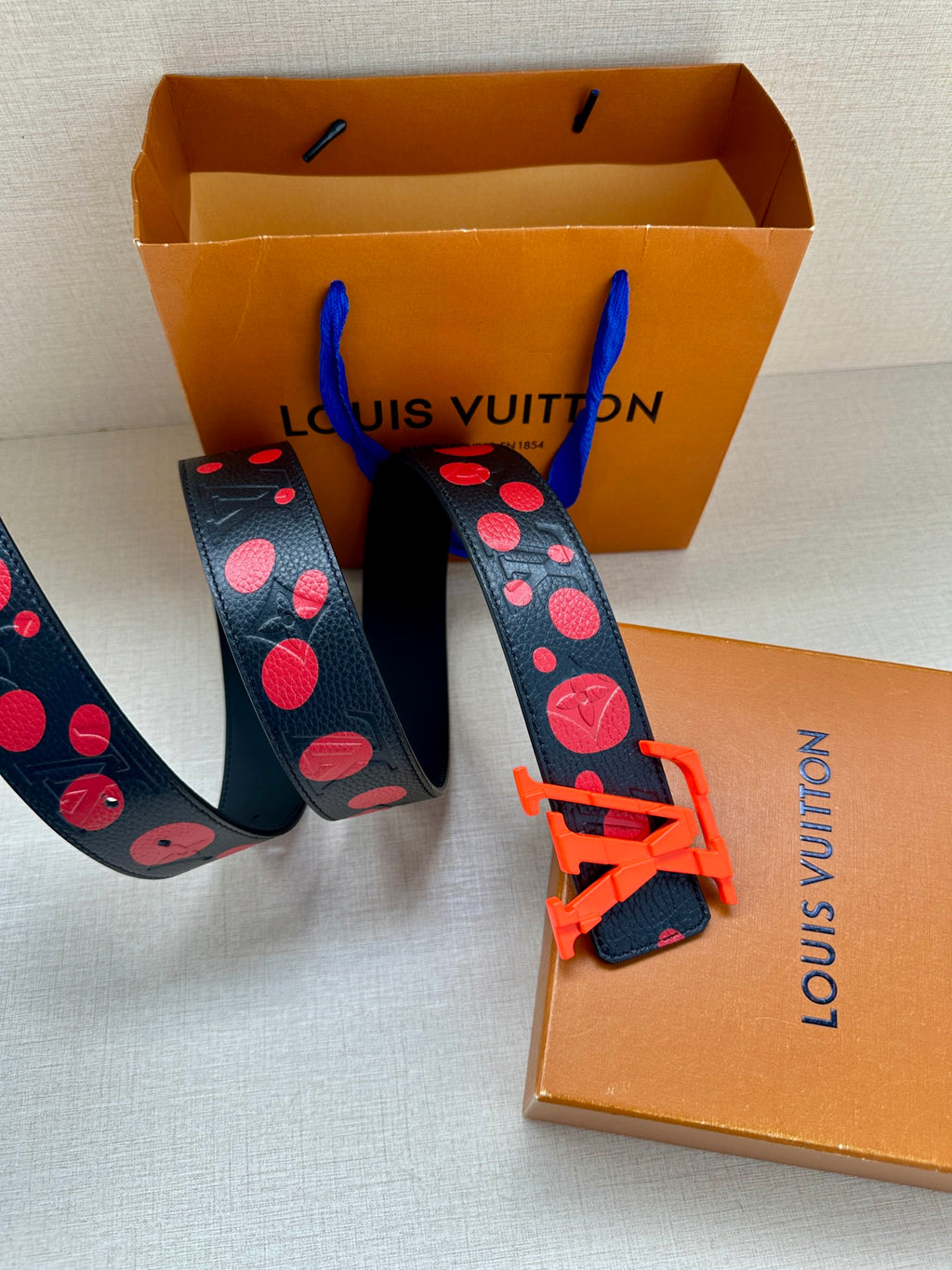 Navy belt with red circle pattern and orange LV buckle on gift box