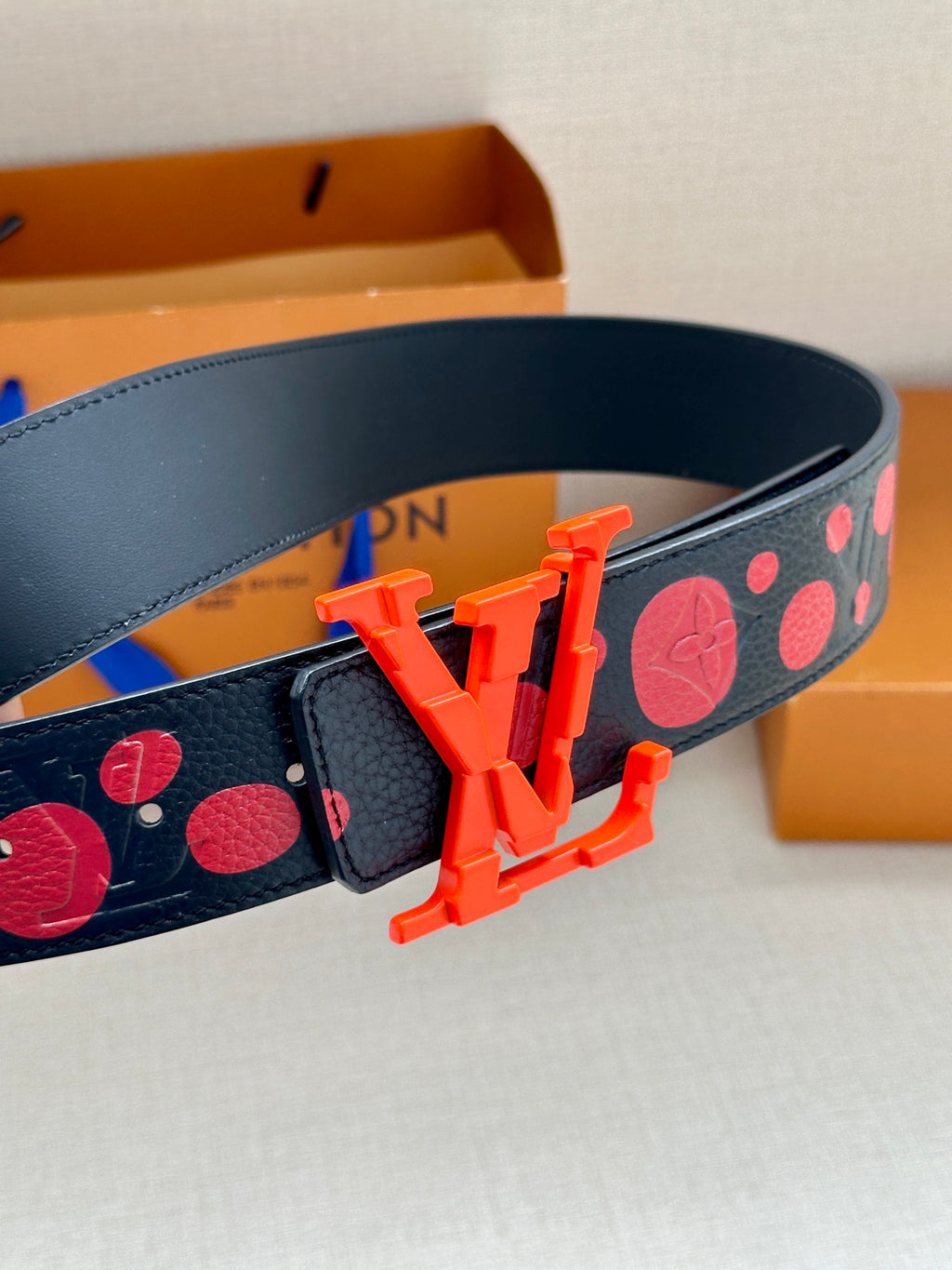 LV logo belt detail: navy strap with red dots and orange buckle hardware