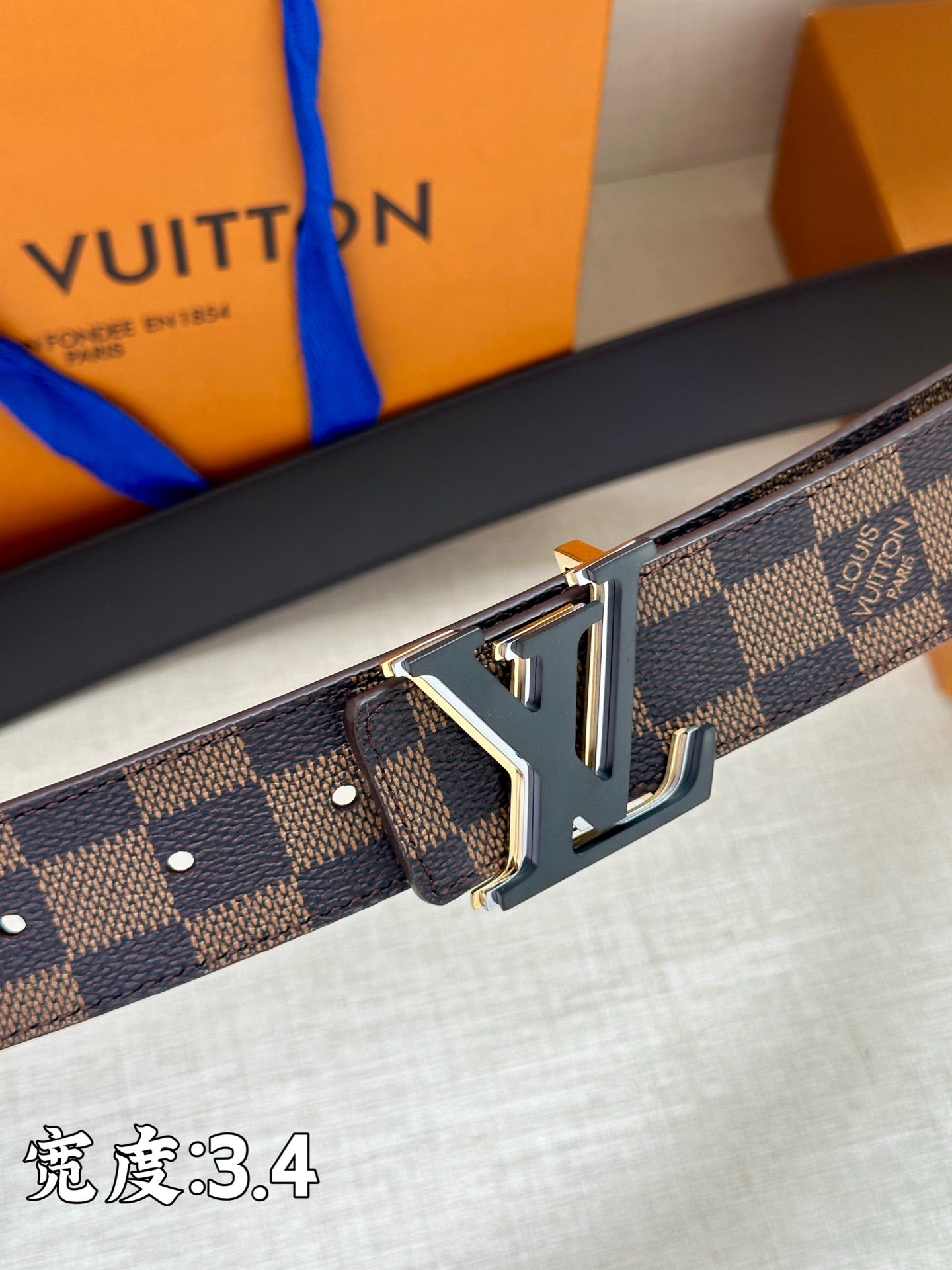 Close-up of checkered leather belt with gold-tone LV buckle and strap holes