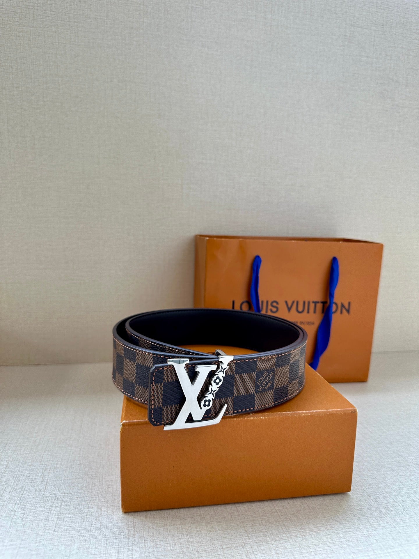 Louis Vuitton belt laid flat: dark check strap with gold LV buckle and black leather edge