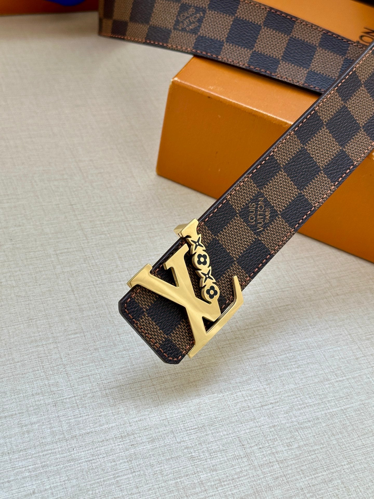 Louis Vuitton belt with dark check pattern strap and gold LV buckle, angled view