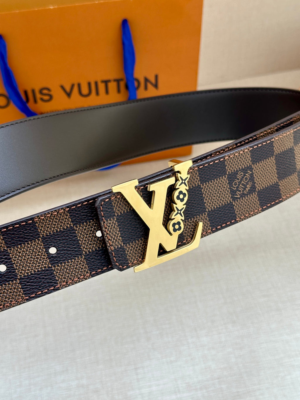 Louis Vuitton belt close-up: dark check strap with gold LV buckle and embossed details
