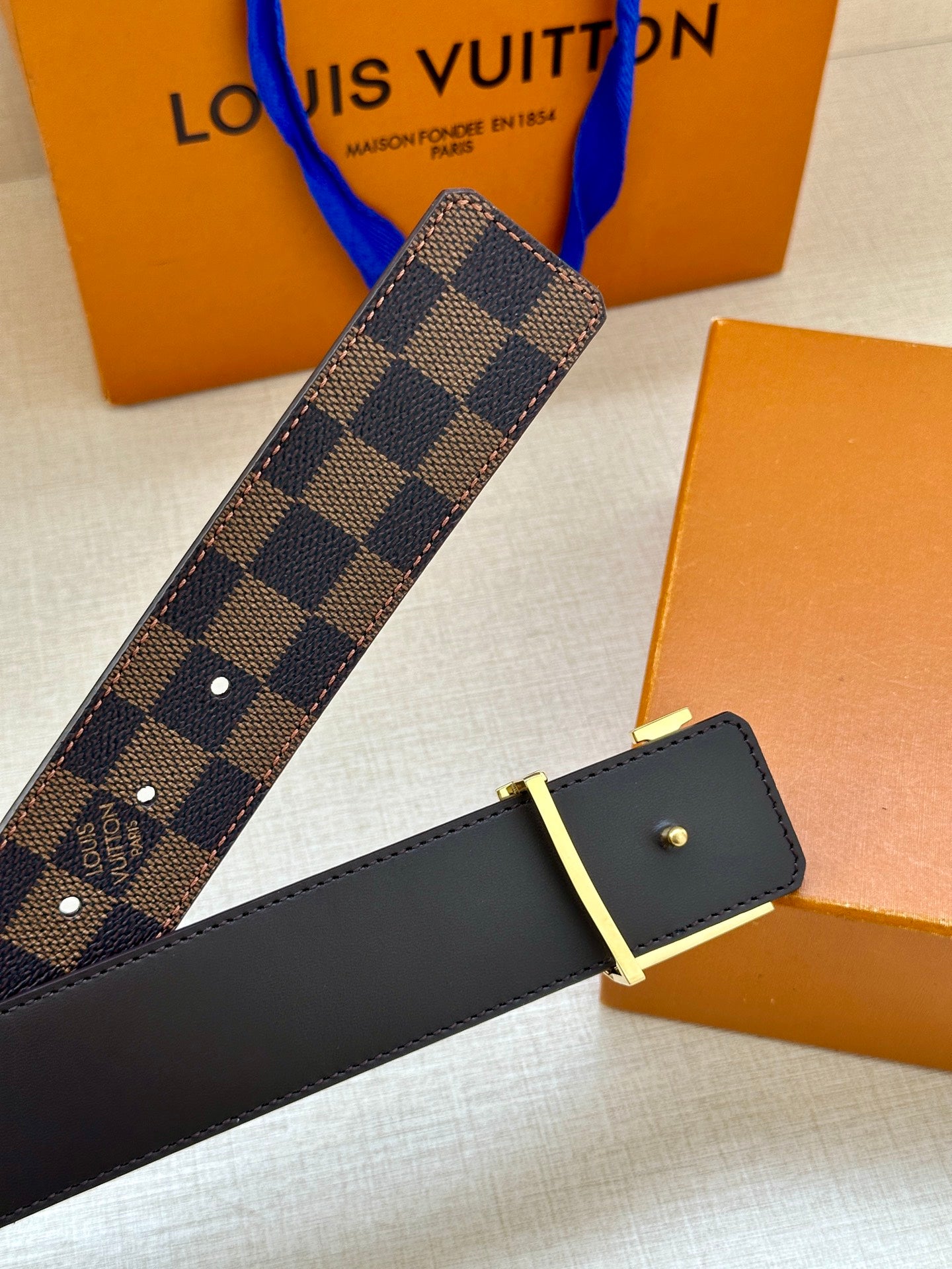 Louis Vuitton belt angled view with dark check strap and gold LV buckle on black leather