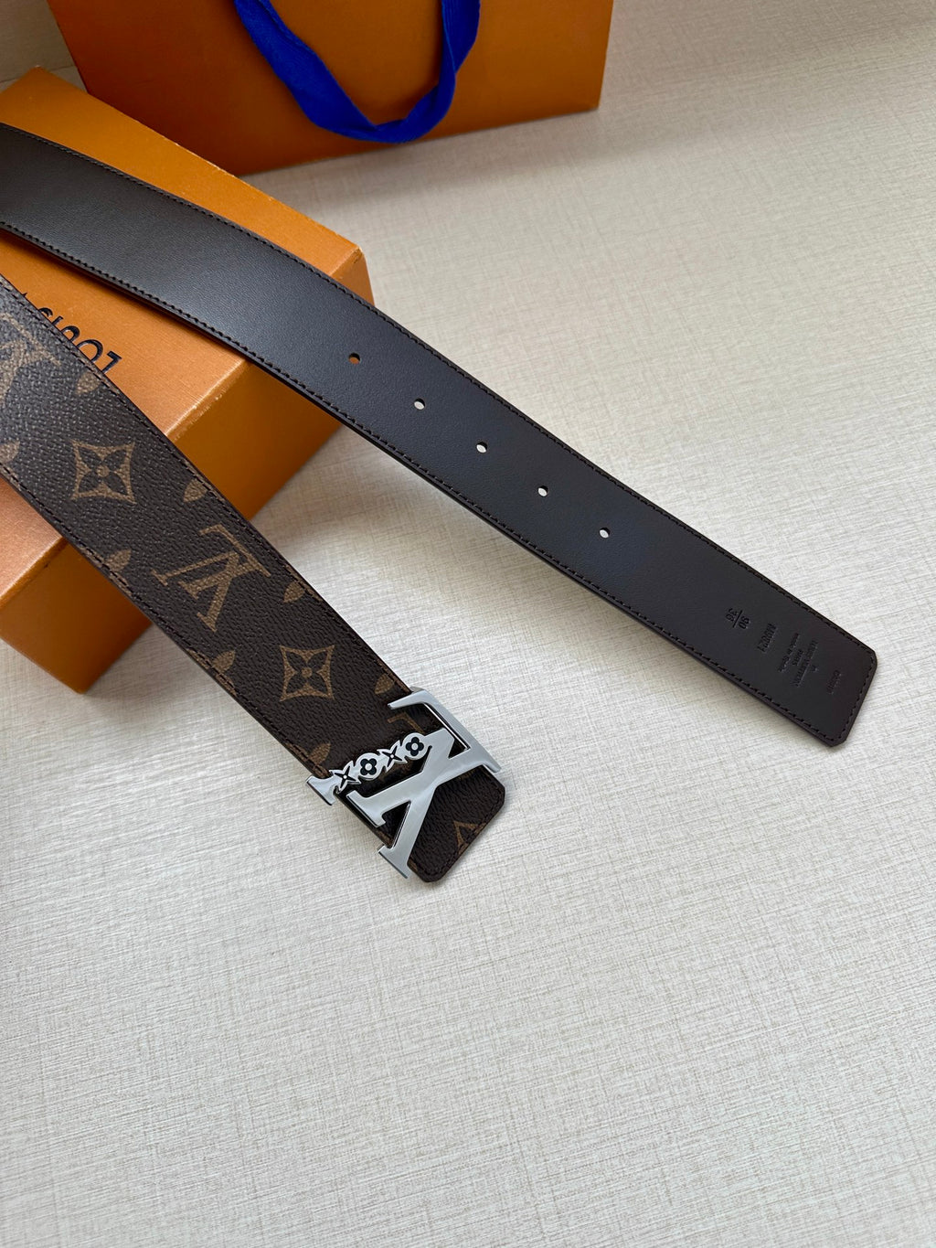 Louis Vuitton belt straps laid out, dark brown monogram with metal buckle