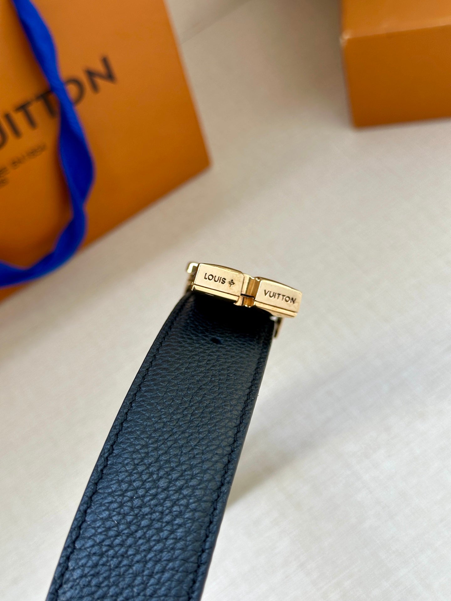 Leather belt close-up: dark blue textured strap with gold LV clasp