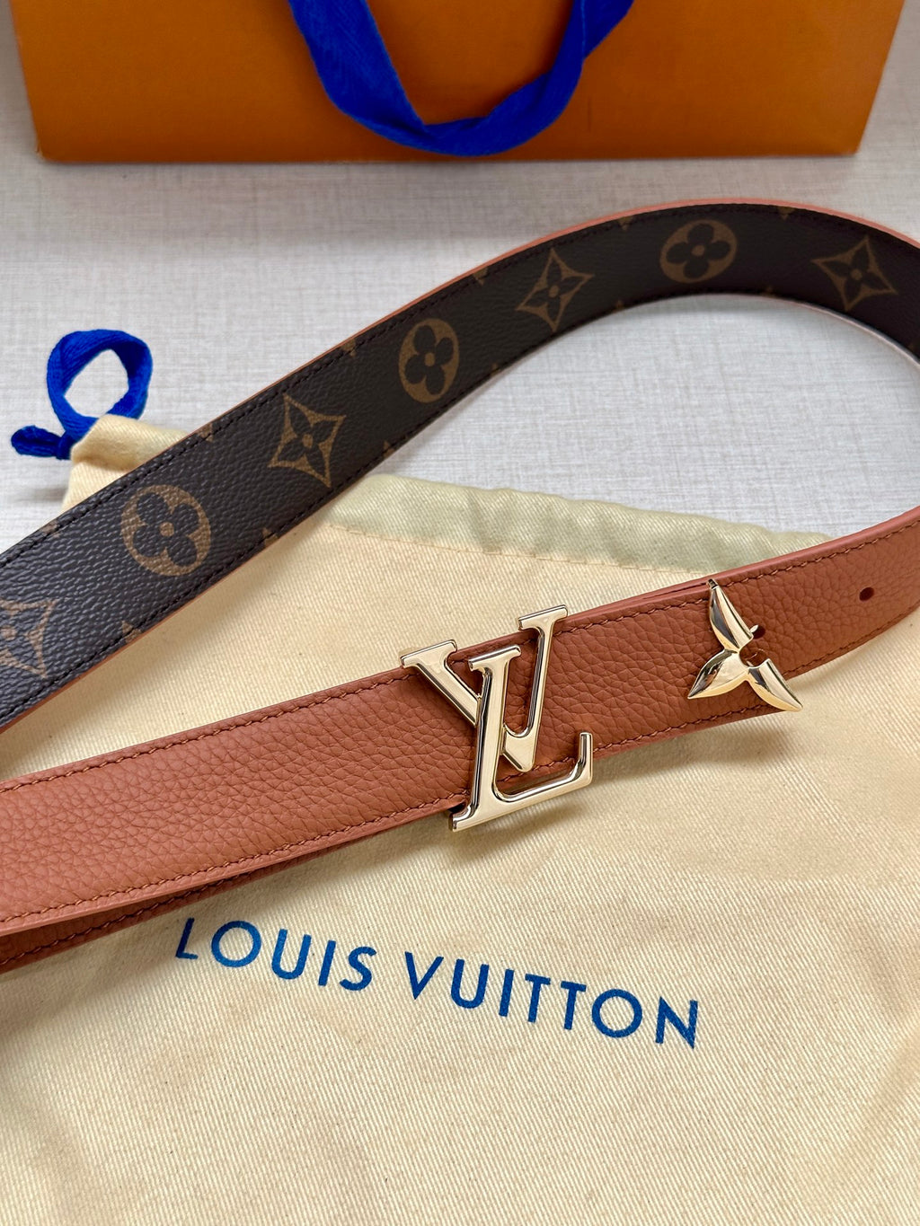 Louis Vuitton belt close-up with monogram strap, tan center, and gold V buckle
