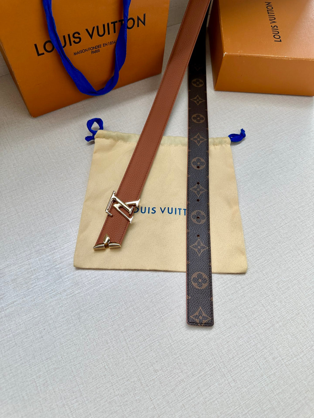 Louis Vuitton belt with dark monogram strap and gold V buckle, on a pouch