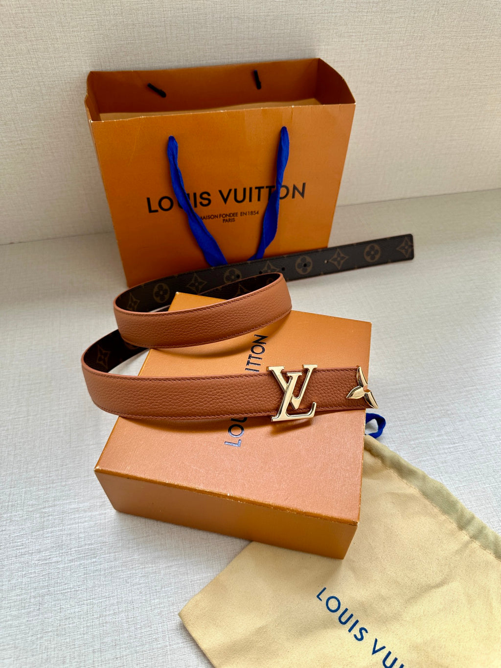 Louis Vuitton belt coiled, featuring tan leather strap and gold buckle with letter V