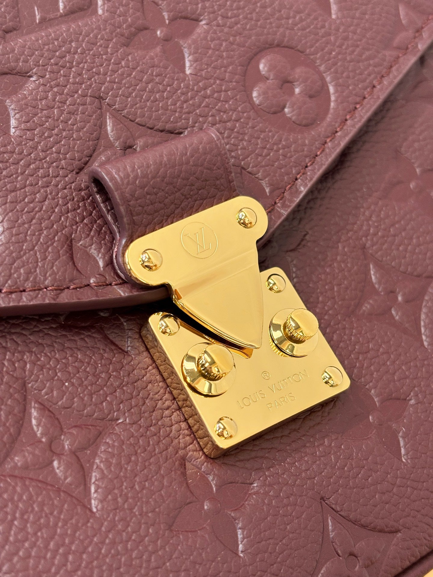 Louis Vuitton mini flap shoulder bag close-up, dark plum embossed monogram, gold lock plate.