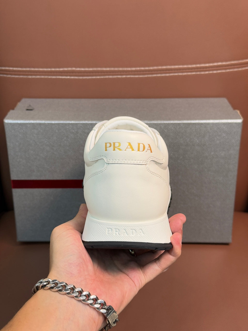 White lace-up sneaker held in hand, Prada logo on heel and tongue