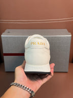 White lace-up sneaker held in hand, Prada logo on heel and tongue