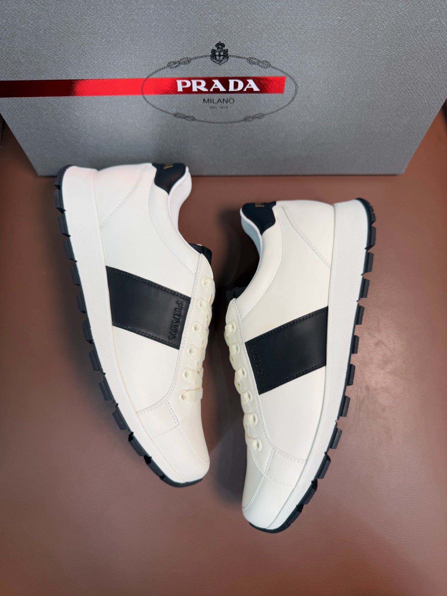 Two white Prada unisex sneakers showing black inset panels and chunky tread sole