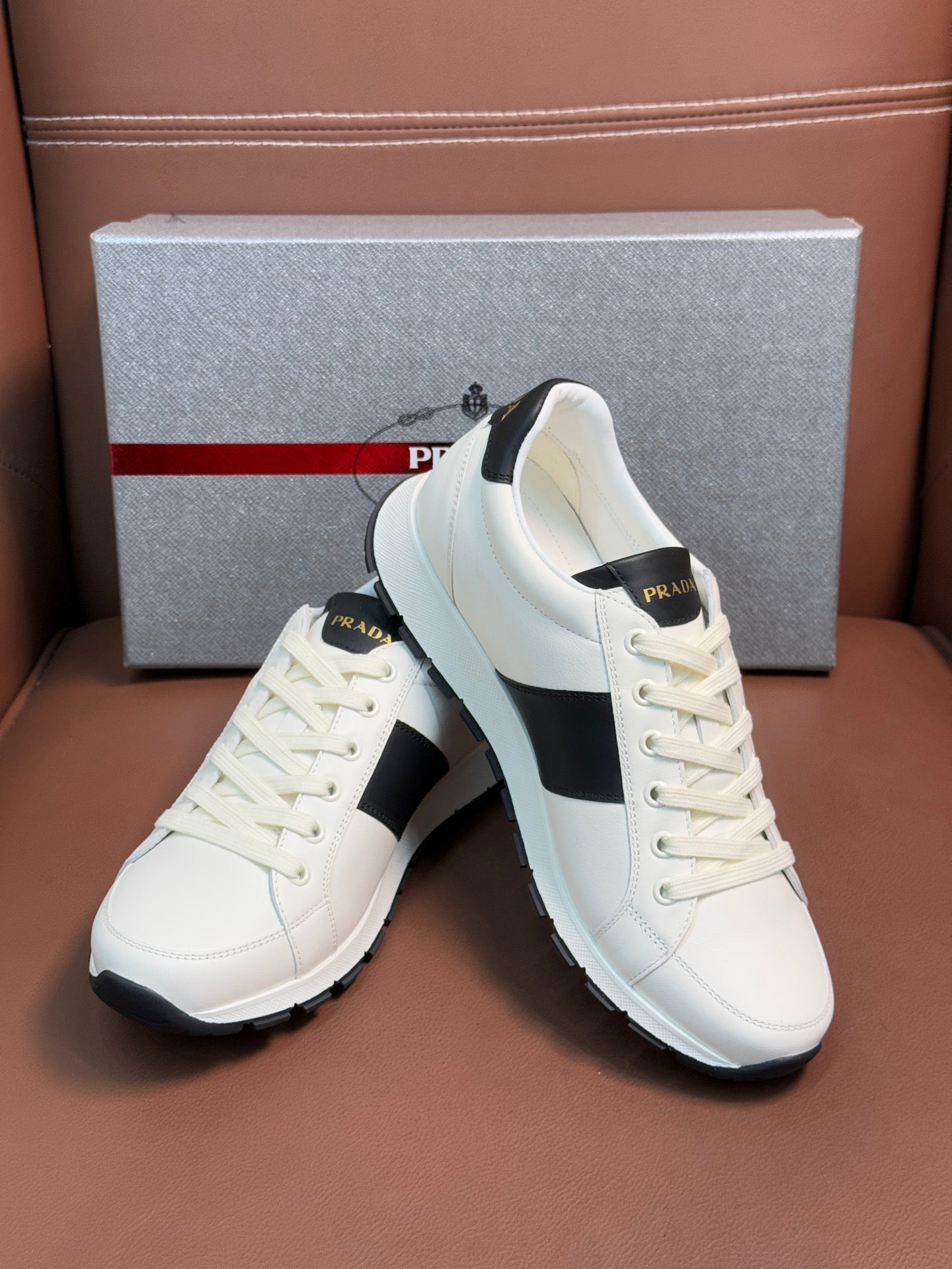 White Prada unisex sneakers with black side panels and white laces, angled view