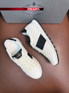 White Prada unisex sneakers with black side panels, one angled sideways