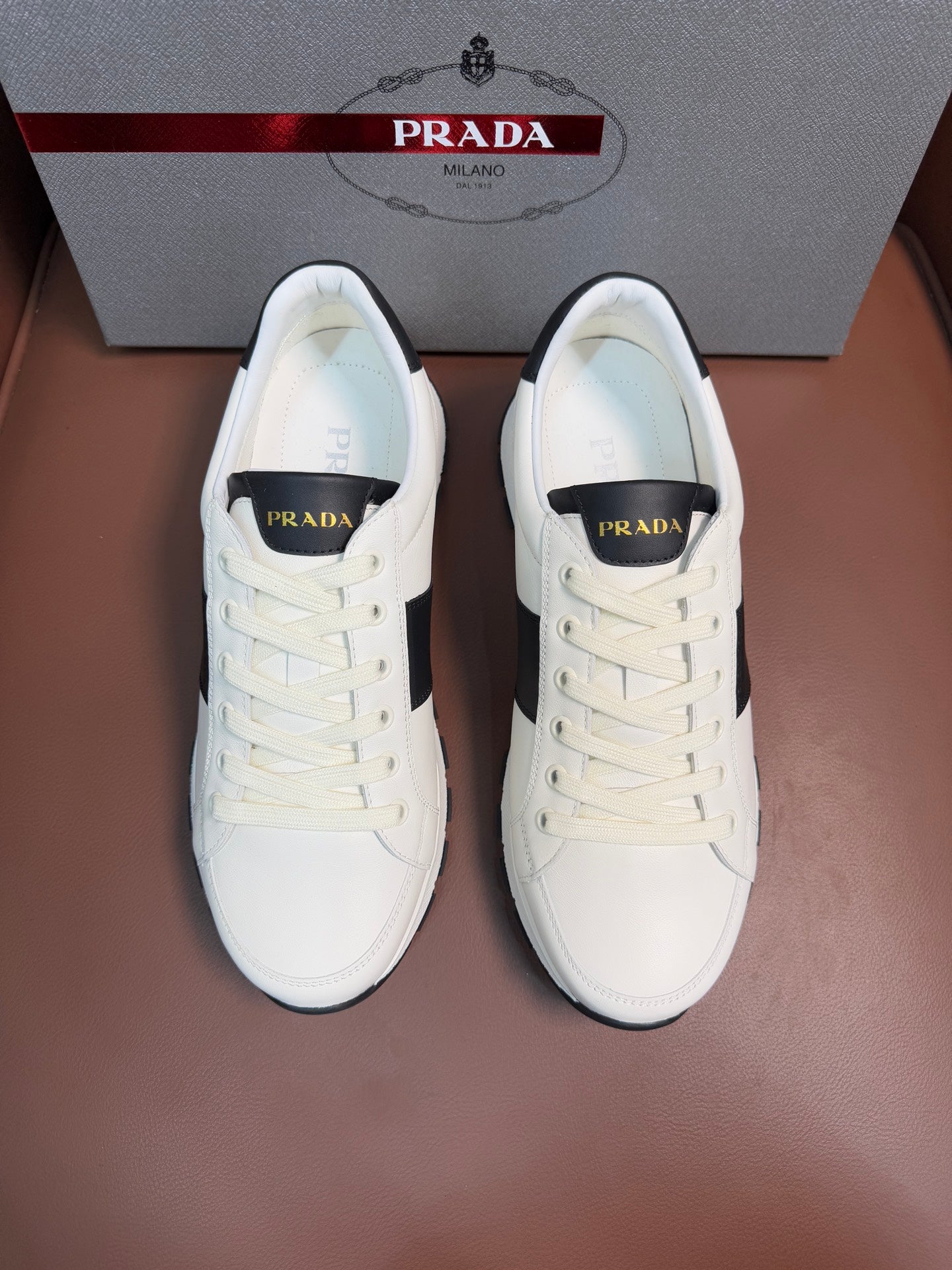 Pair of white Prada unisex sneakers with black side panels and lace-up design
