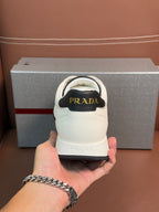 White Prada unisex sneaker heel close-up held in hand; black interior panel