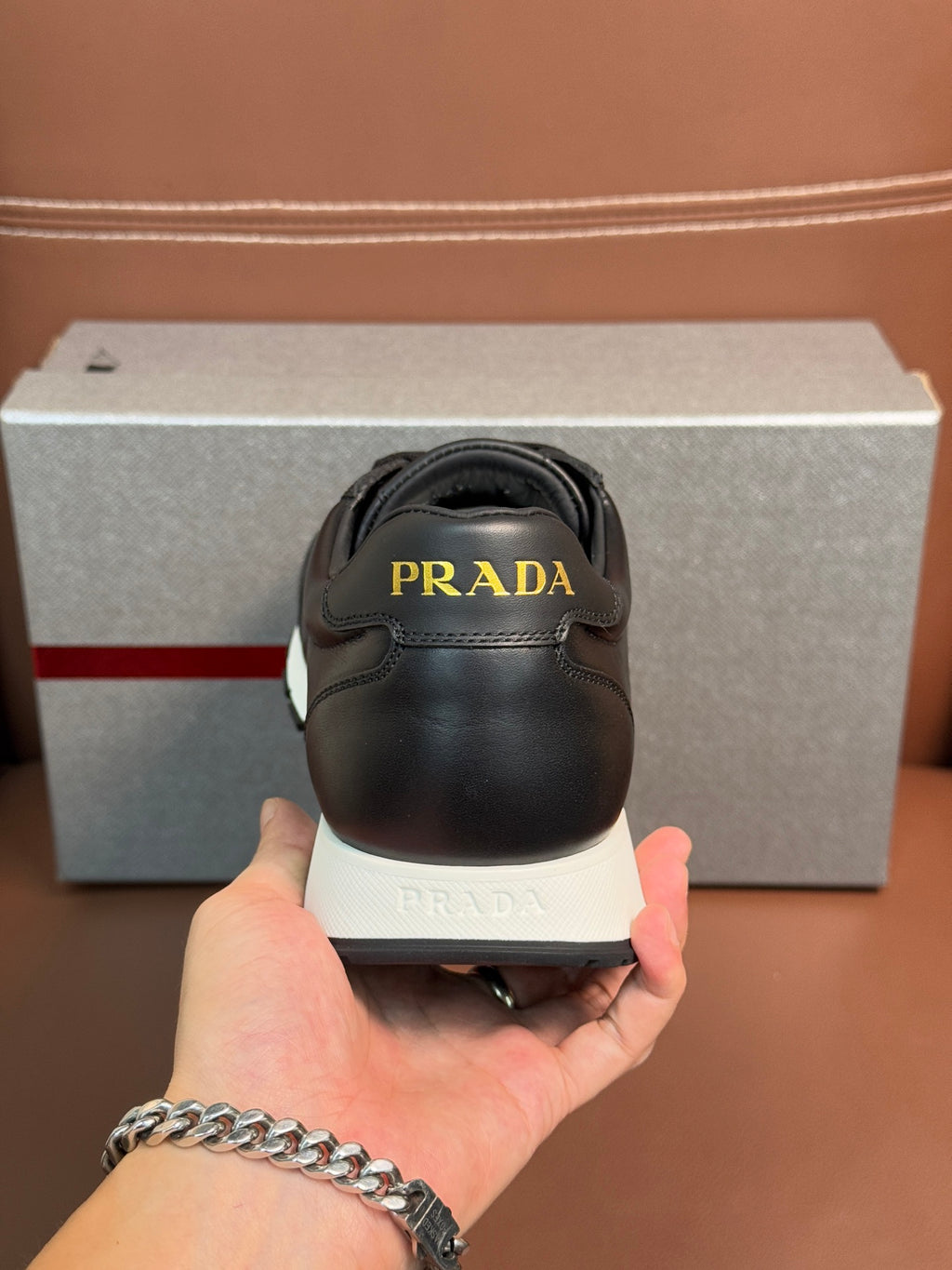 Prada unisex sneaker heel close-up, dark leather with logo on back and white sole