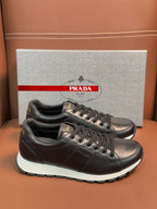 Prada unisex sneakers pair on the box, dark leather lace-up with white midsole trim