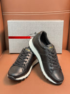 Prada unisex sneakers pair shown with box, dark leather lace-up and thick white sole