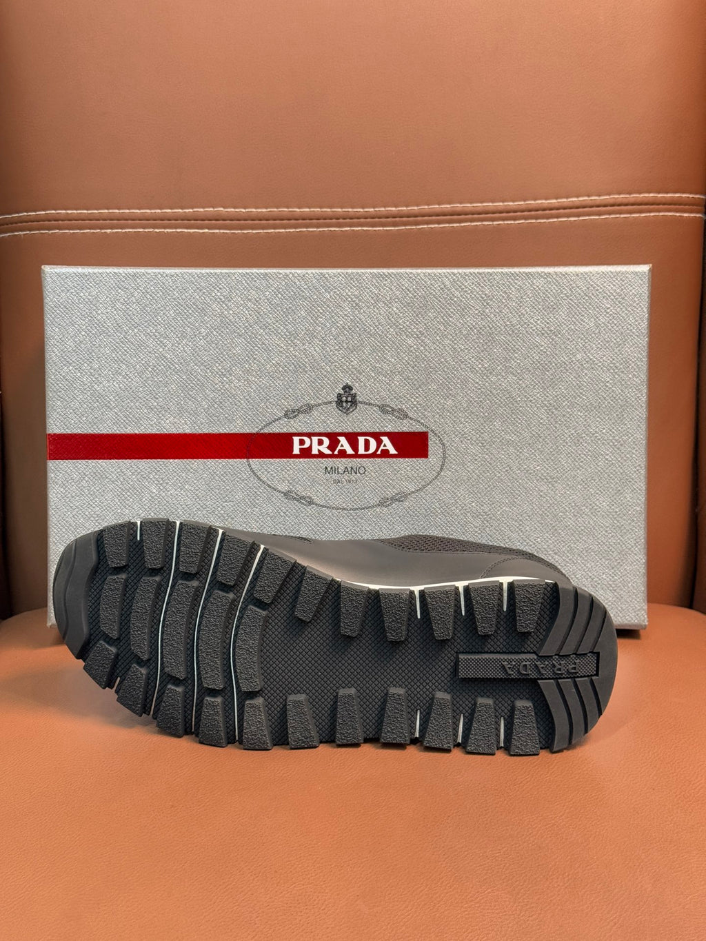 Prada unisex sneaker outsole view, dark rubber tread with brand detail