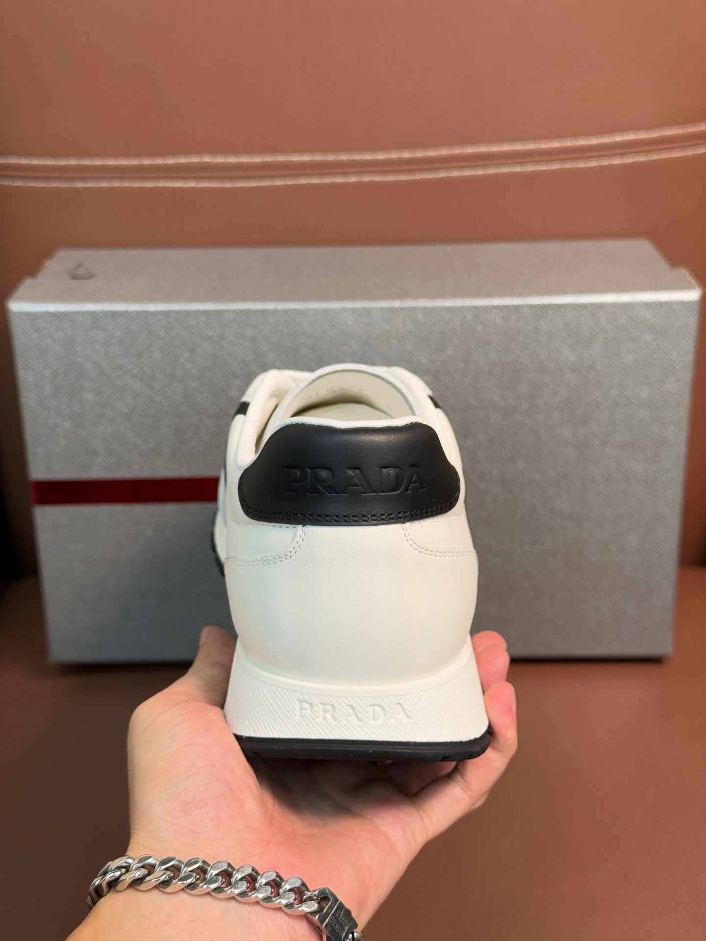 White unisex sneaker heel with black trim and Prada logo, held in hand