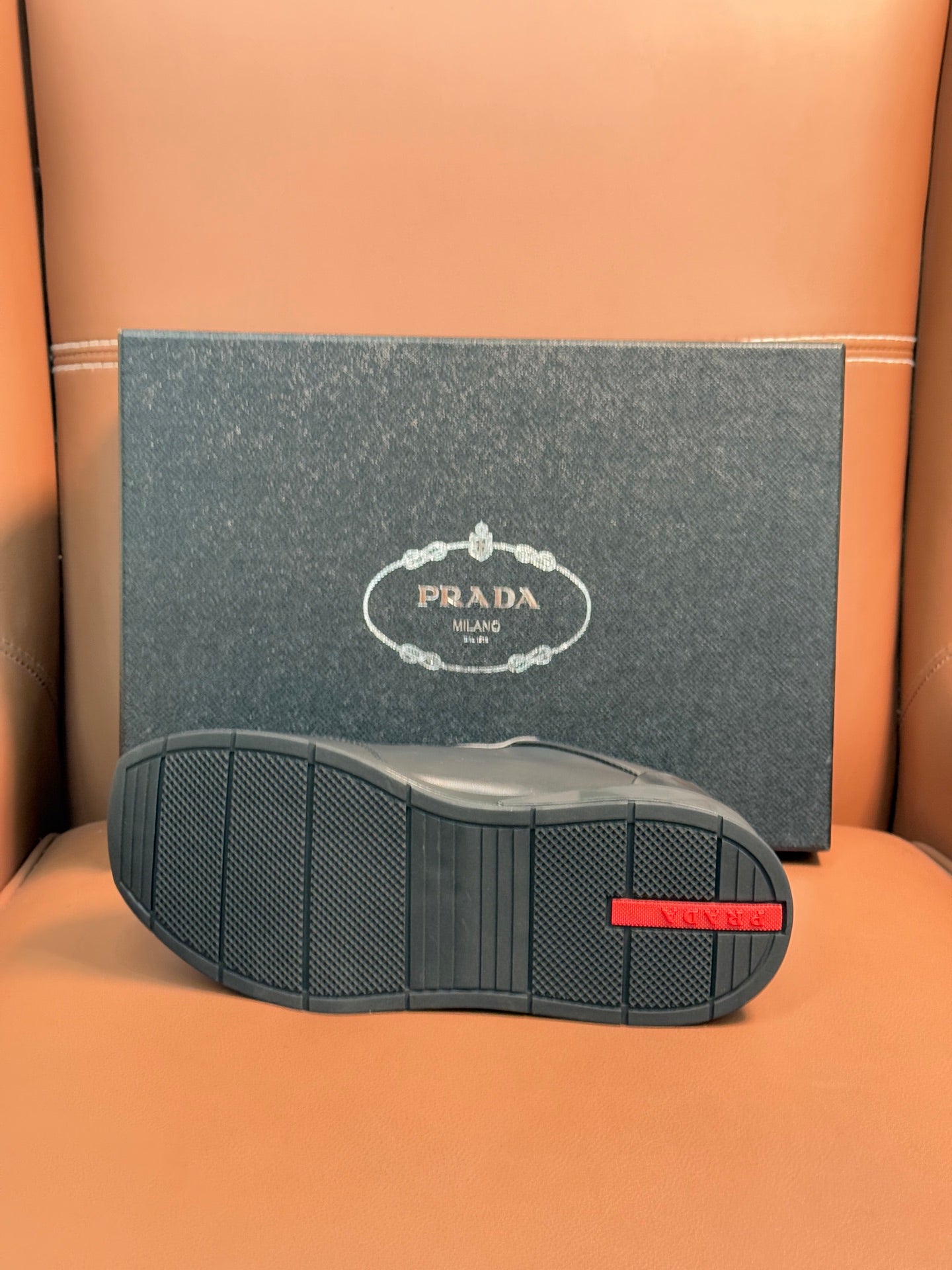Prada dark sneaker outsole with textured tread and red brand stripe
