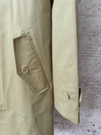 Tan coat side view with angled buttoned pocket and buttoned cuff.