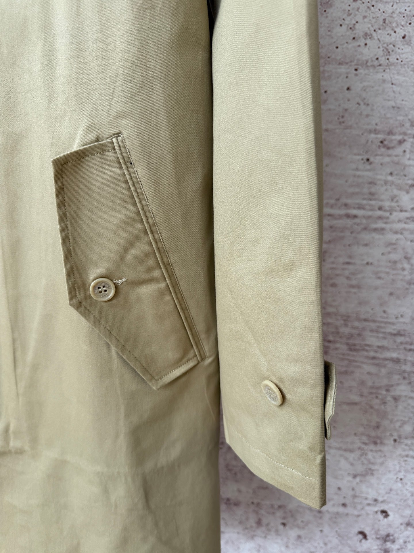 Tan coat side view with angled buttoned pocket and buttoned cuff.
