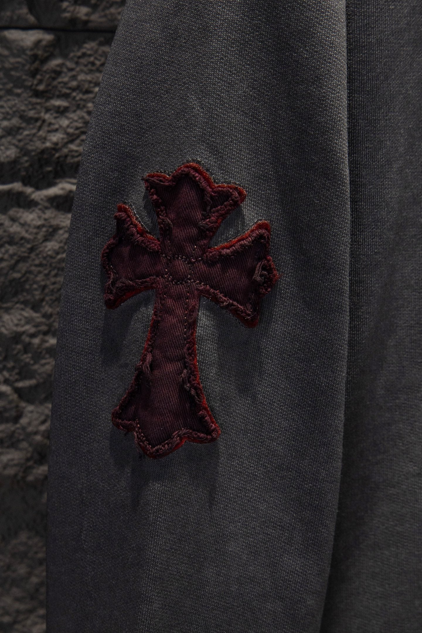 Cross applique on dark gray hoodie sleeve with maroon outline