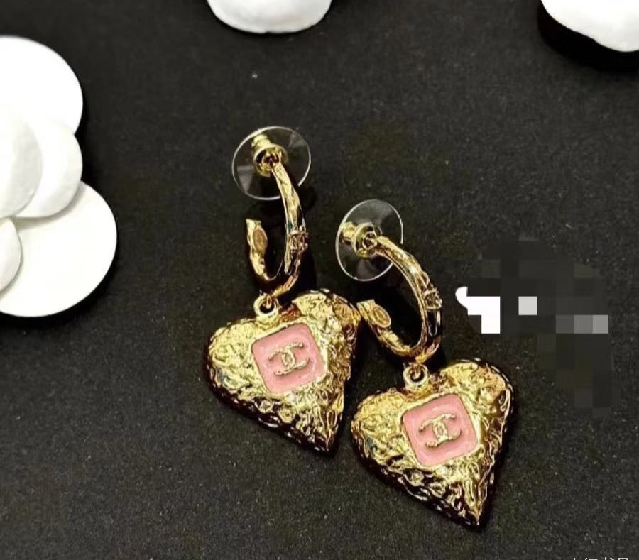 Gold-tone heart drop earrings with pink enamel logo on dark display fabric.