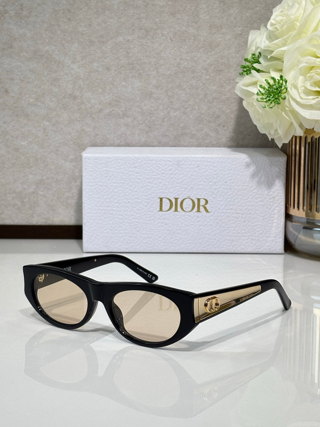 Dior sunglasses with black round frames and neutral lenses, gold logo bar on temple