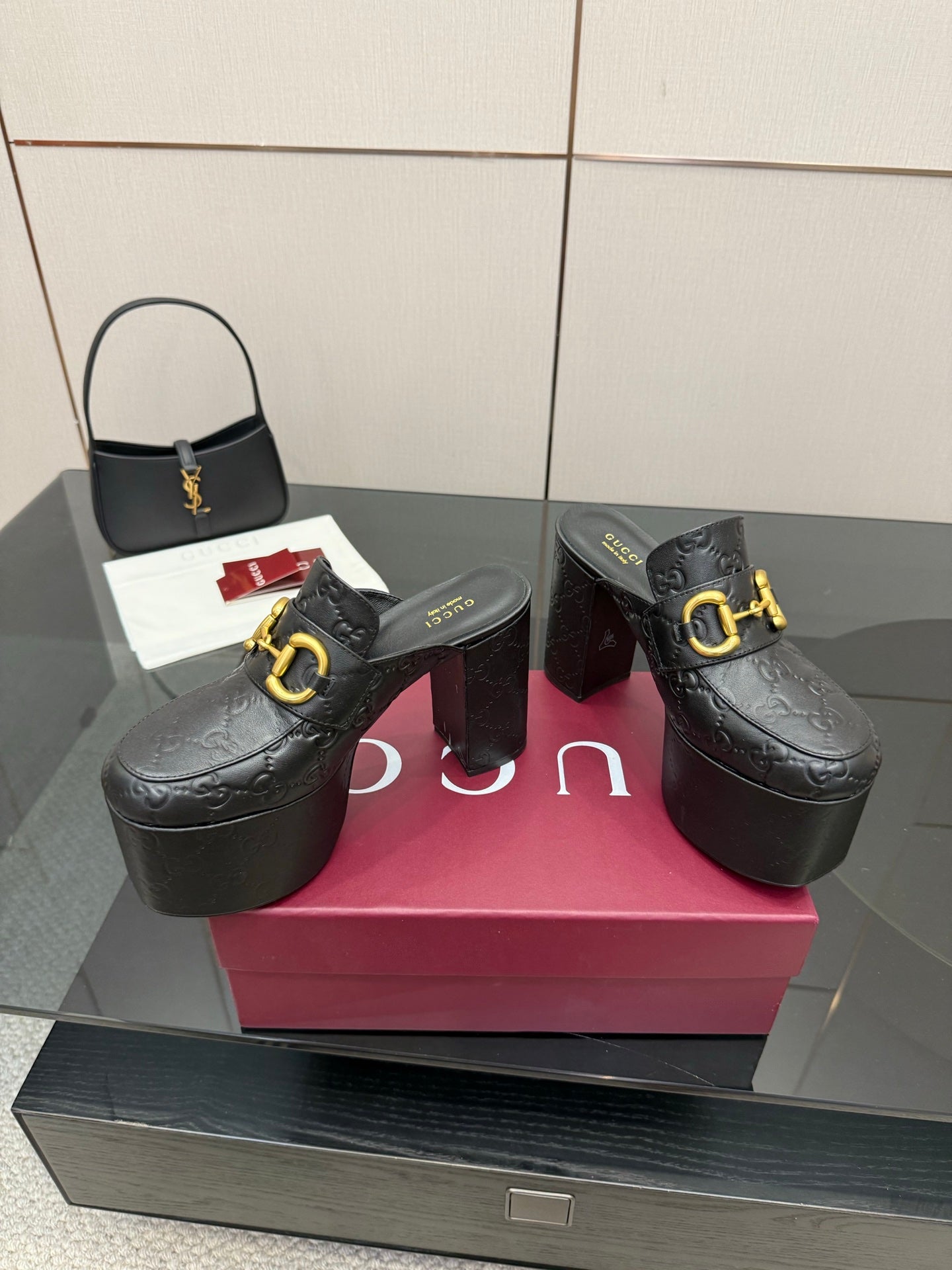 Pair of black Gucci platform mules with gold buckle and textured logo pattern