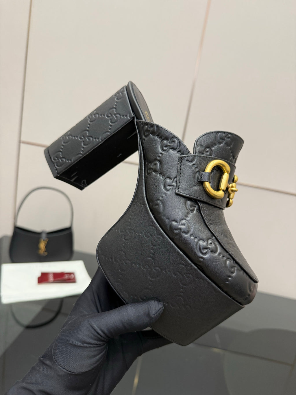 Close-up of black Gucci platform mule with gold buckle strap and logo embossing