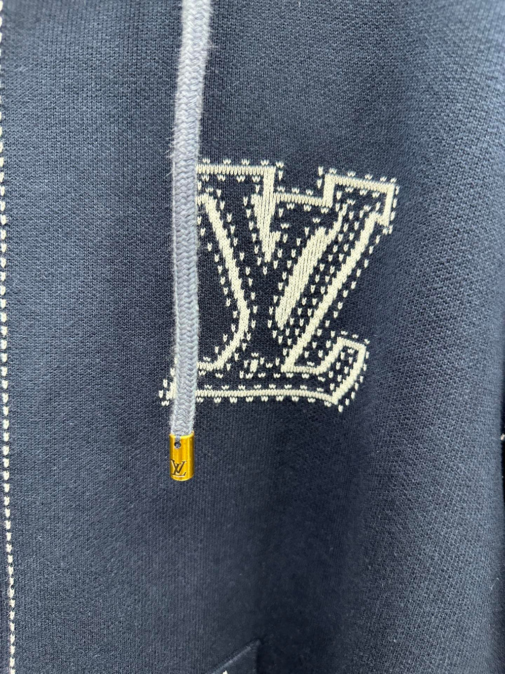 Close-up of navy hoodie chest logo patch with yellow zipper pull and drawstring