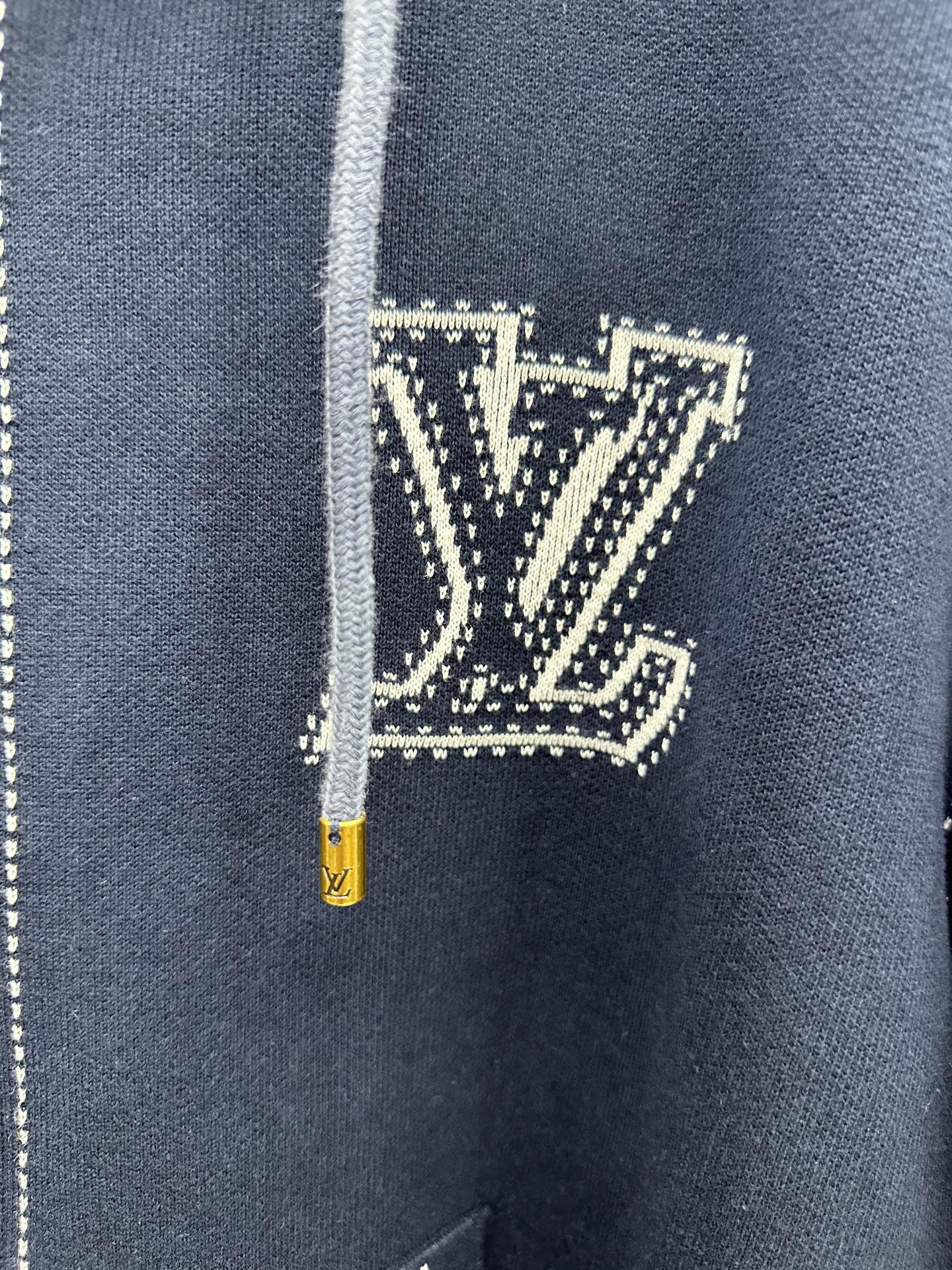 Close-up of navy hoodie chest logo patch with yellow zipper pull and drawstring