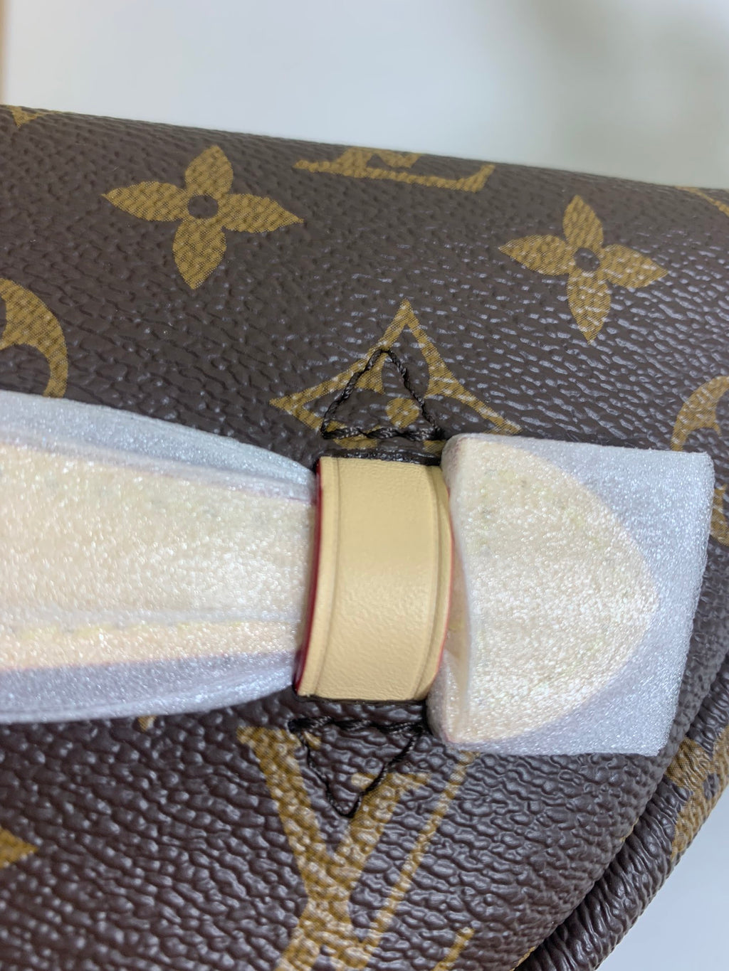 Louis Vuitton monogram bag detail: cream bow with buckle and tan leather strap