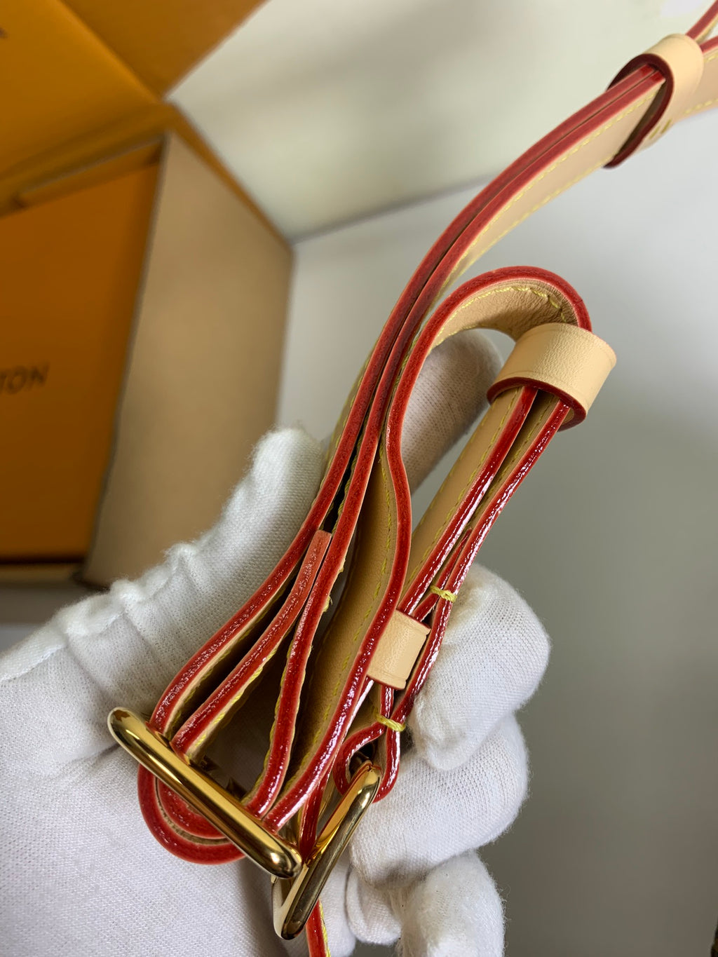Louis Vuitton strap detail with red trim, tan strap and gold ring hardware