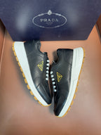 PRADA low-top sneakers, dark leather with white laces, off-white panels, yellow sole
