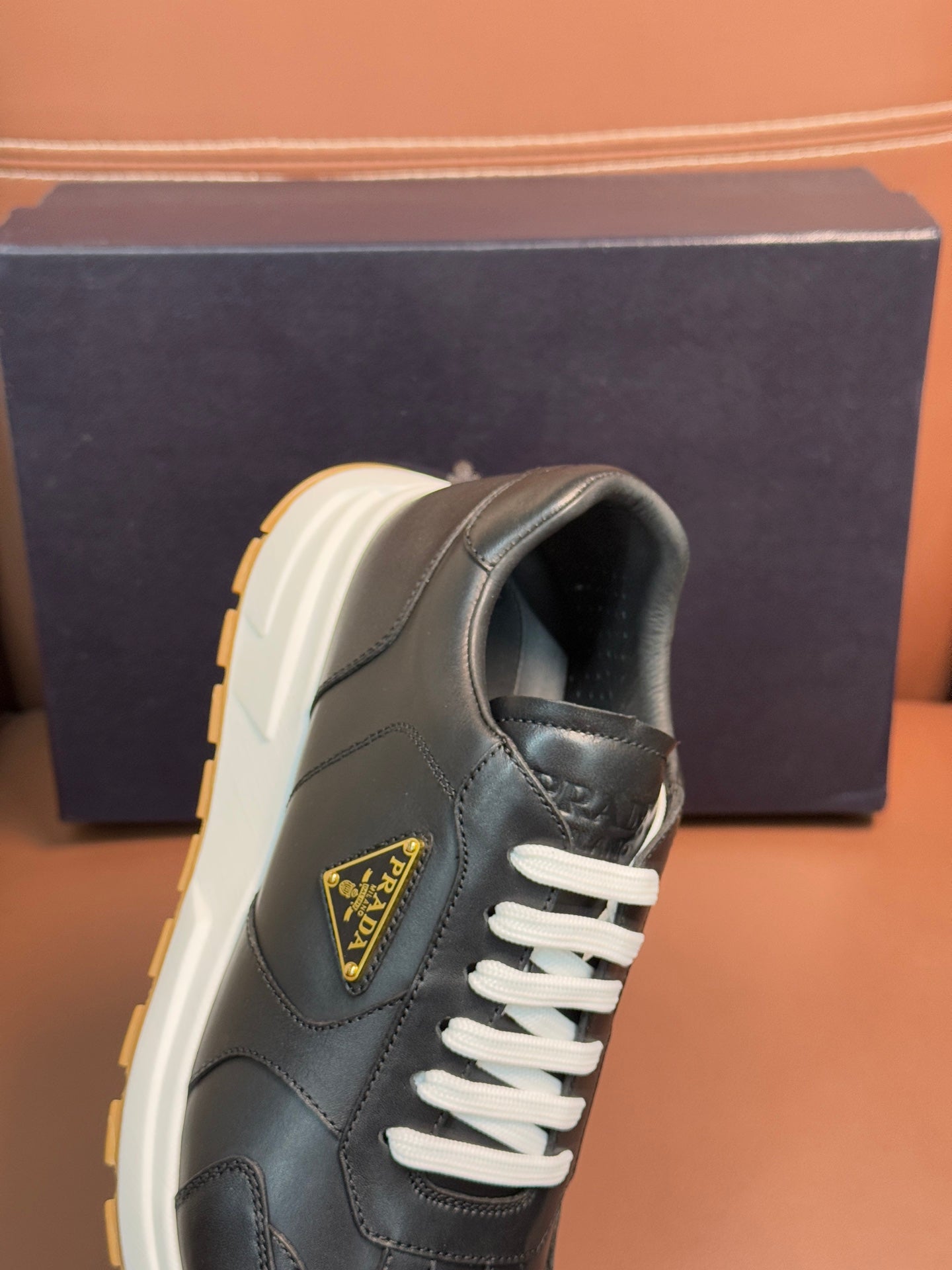 PRADA sneaker side and heel, dark leather, white laces, yellow-trim sole, logo patch