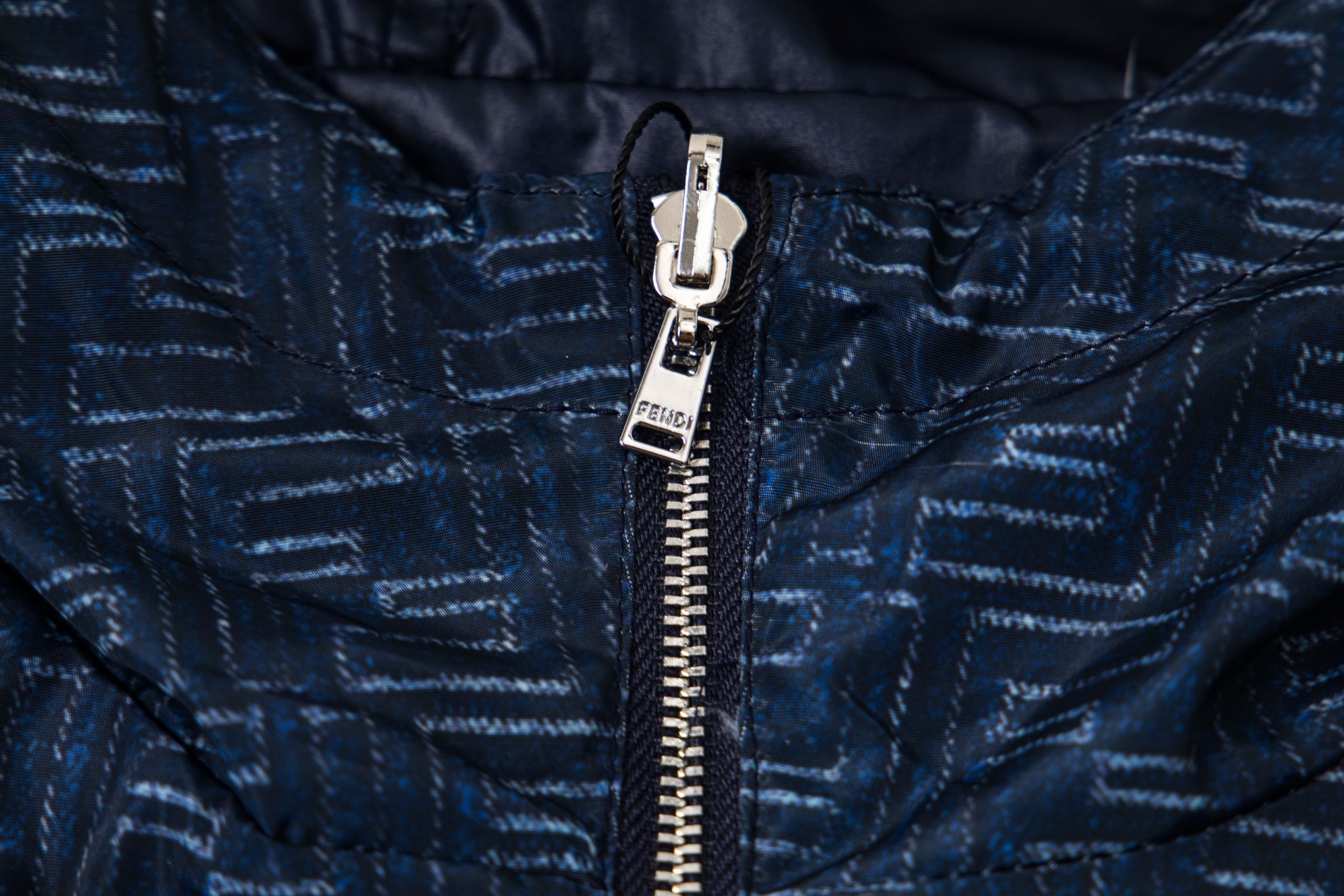 Close-up of metal zipper and hood drawstring on patterned navy jacket