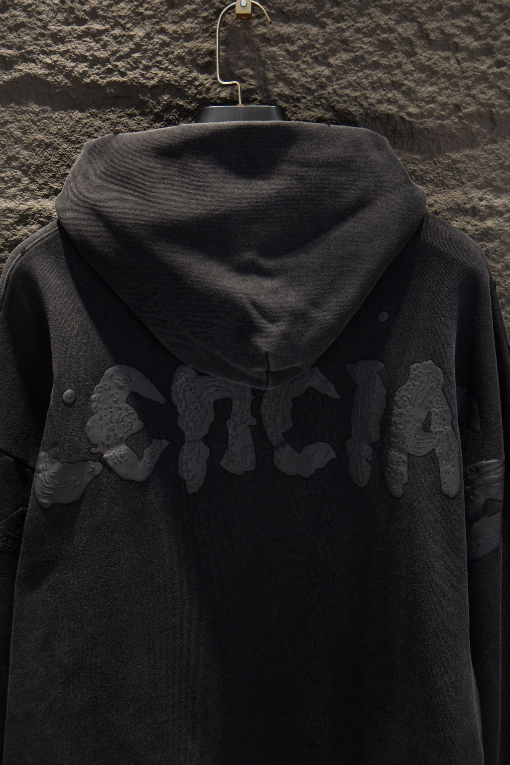 Balenciaga long zip-up hoodie back view, dark with hood and raised graphic lettering.