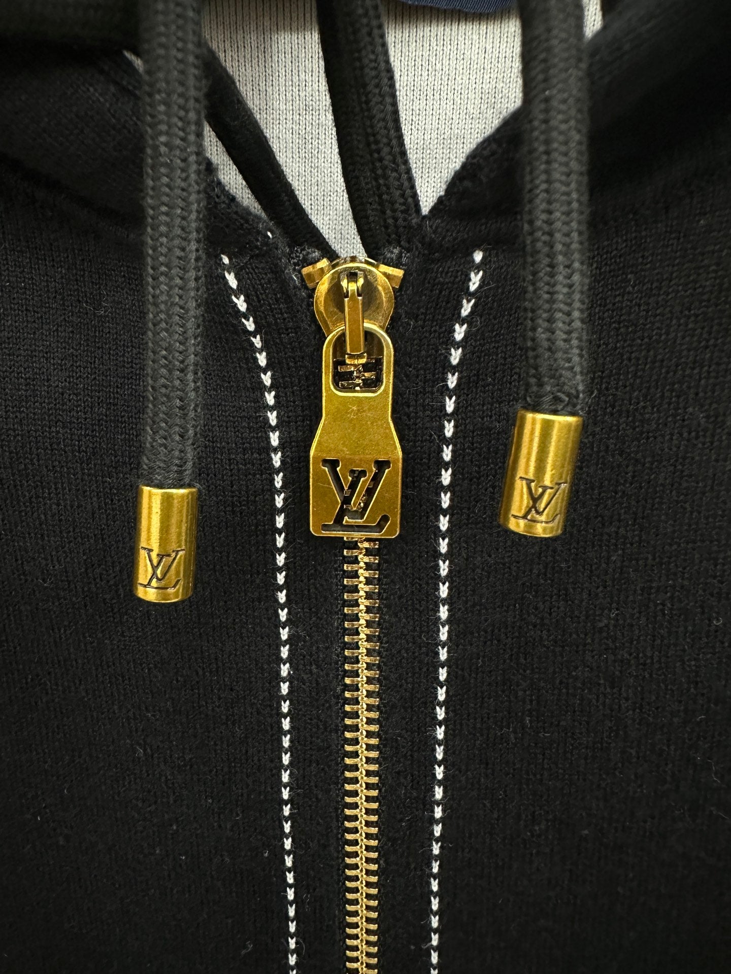 Close-up of gold zipper pull and LV emblem on a black hoodie