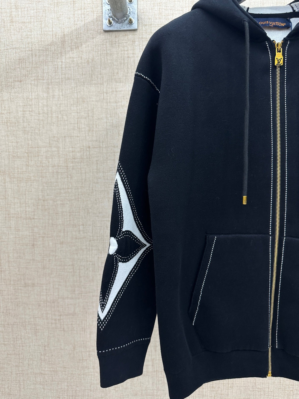 Zip-up hoodie sleeve with black-and-white diamond logo graphic and gold zipper