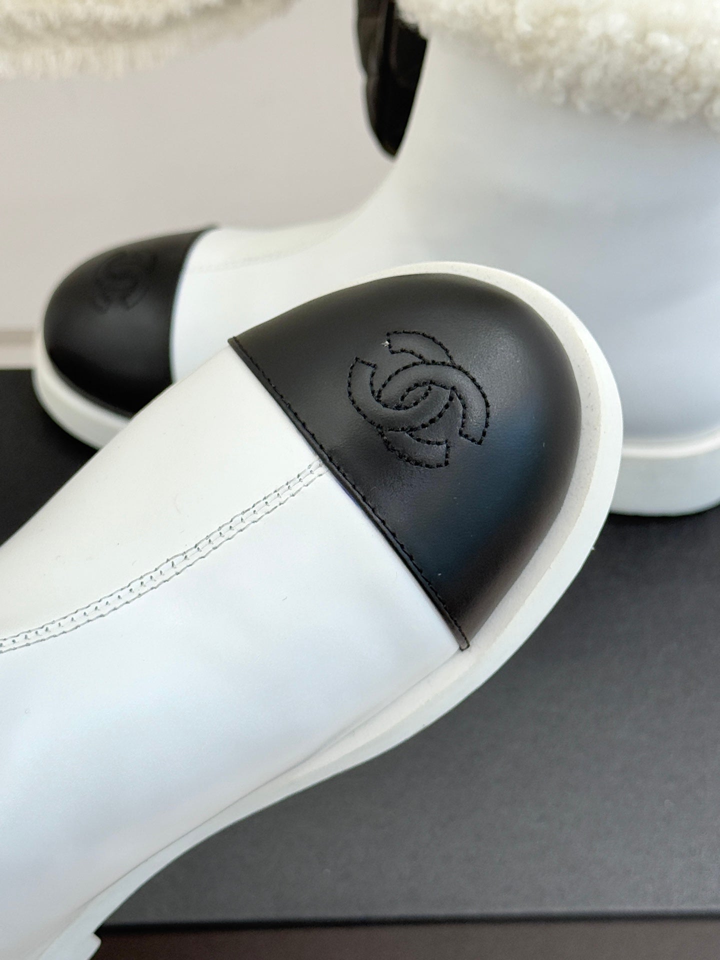 White women's slip-on ankle boot with black toe panel and embossed logo